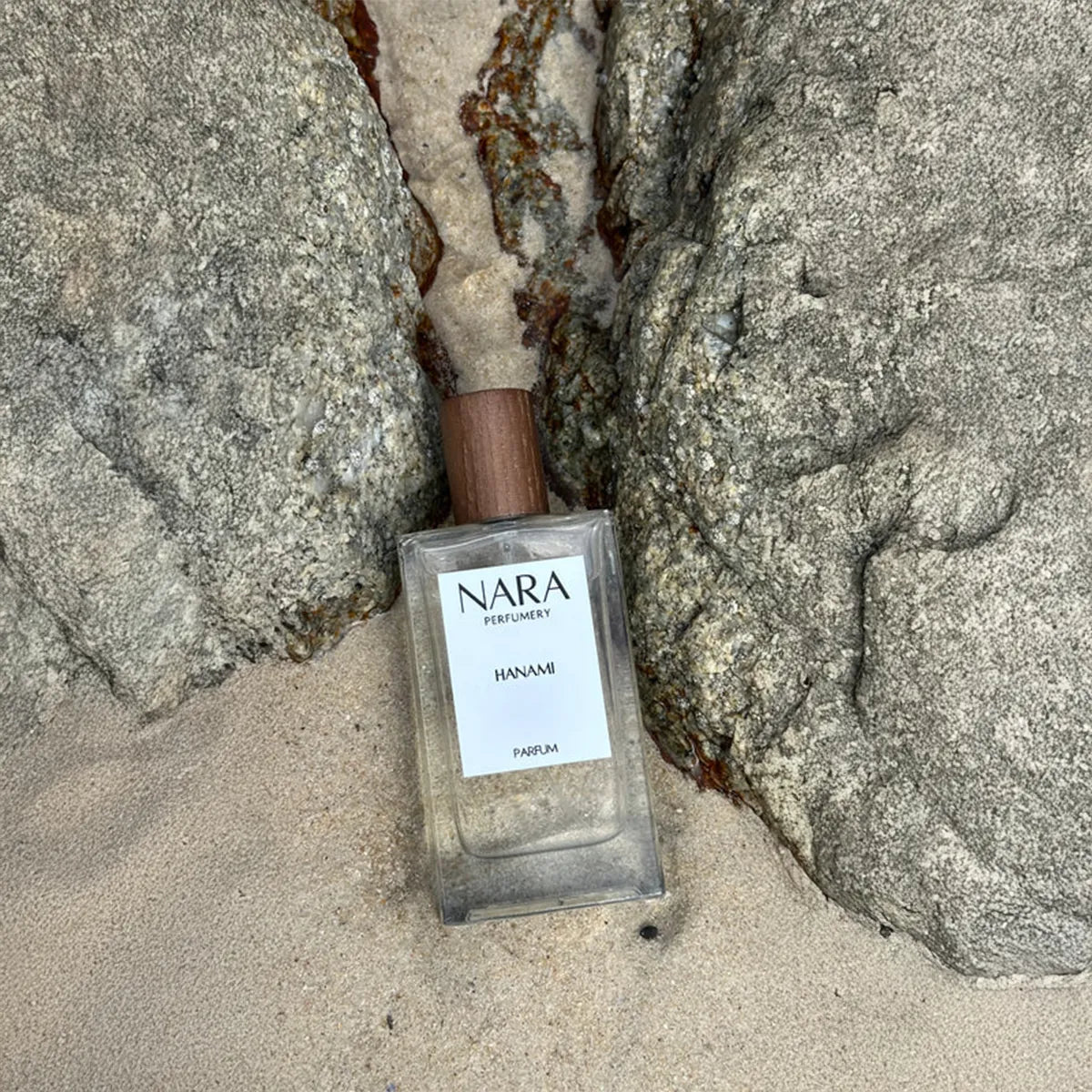 Nara perfume bottle on sand with rocks in the background