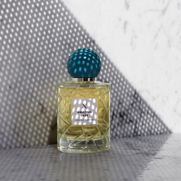 Perfume bottle labeled 'Amazing Jade' with a textured blue cap on a metallic surface.
