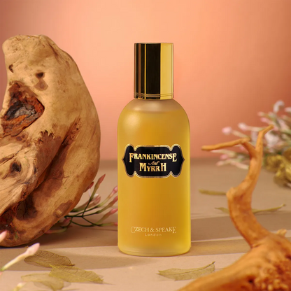 Bottle of Frankincense and Myrrh perfume by Czech & Speake with decorative elements on a peach background
