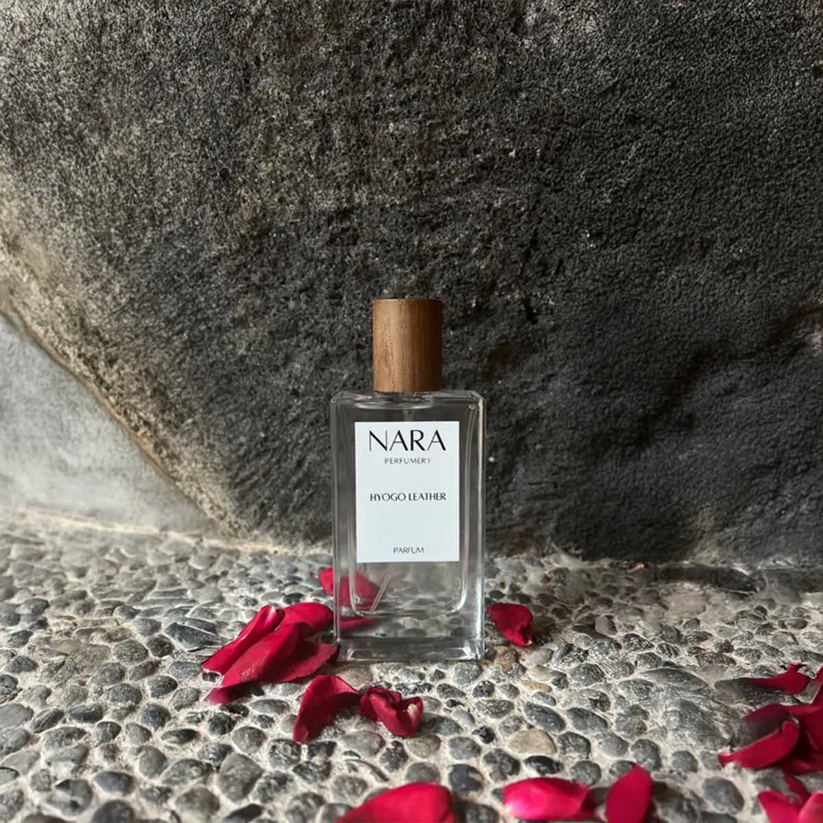 NARA perfume bottle with wooden cap on a stone surface with red petals