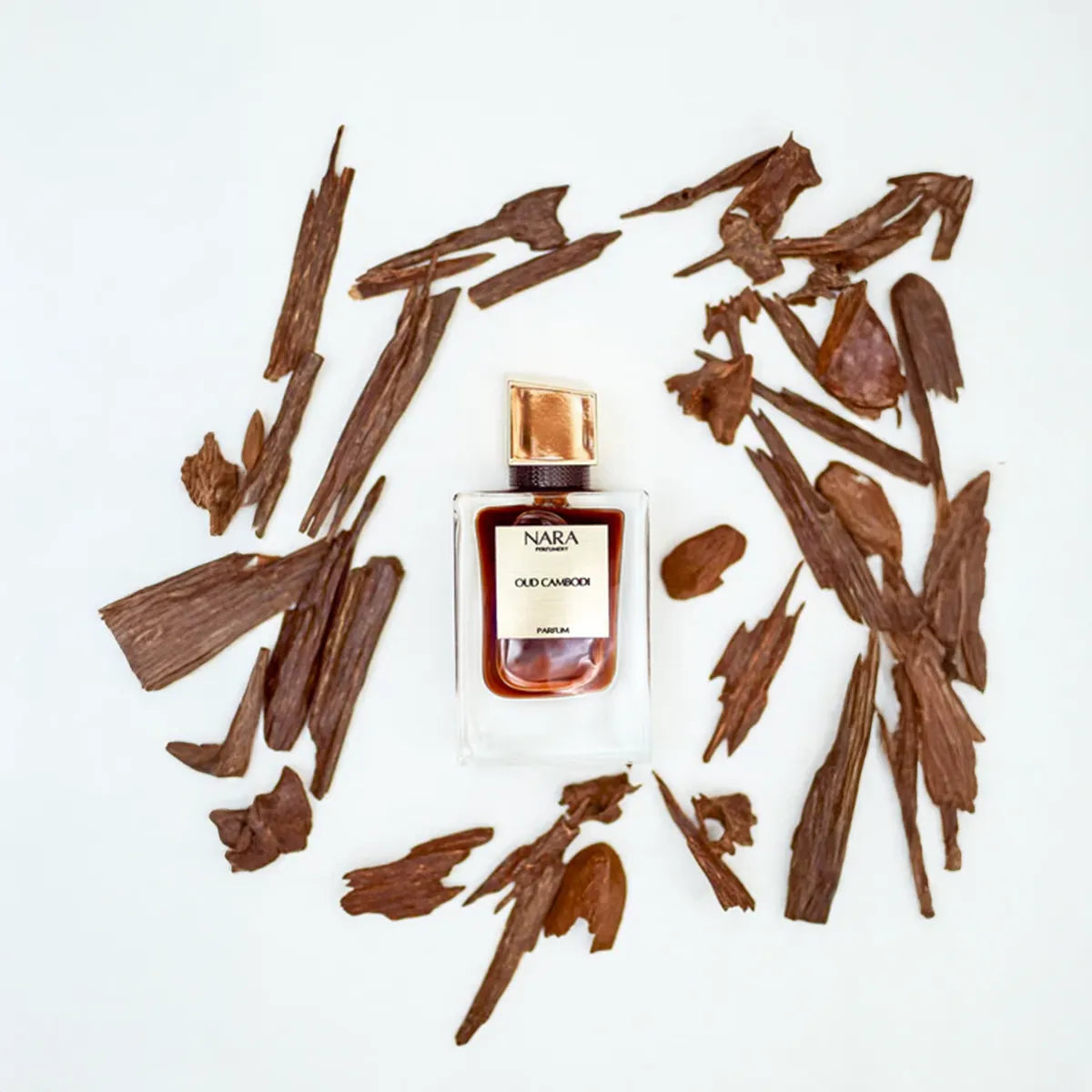 NARA Oudh Chandan perfume bottle surrounded by dried wood pieces on a white background