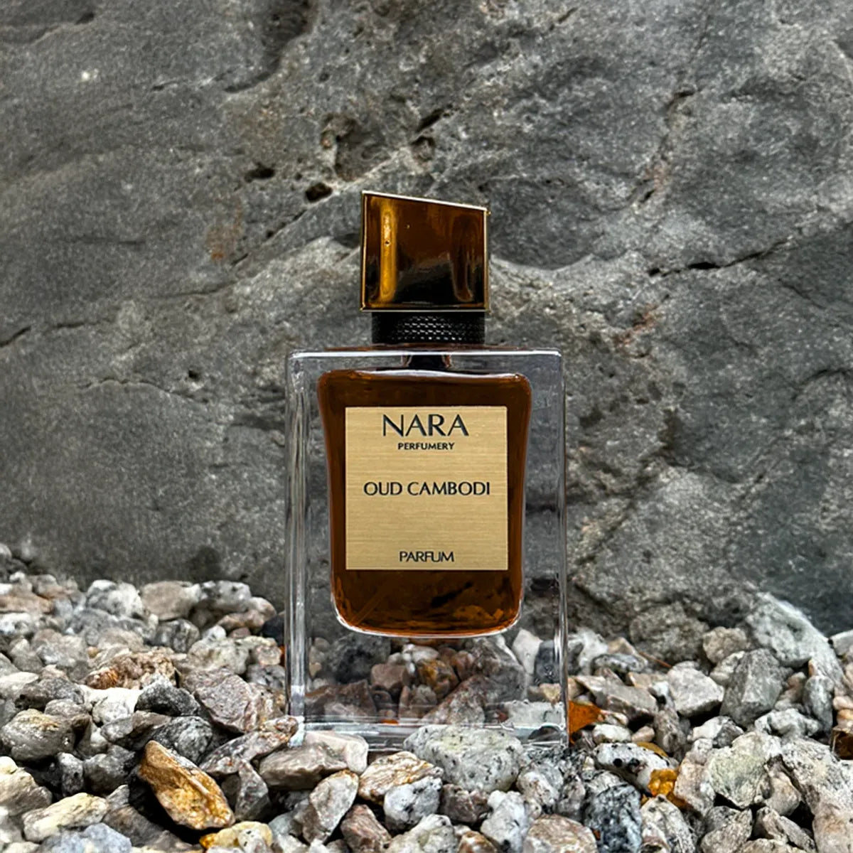 Nara Oud Cambodi perfume bottle on a rocky surface with a stone wall background