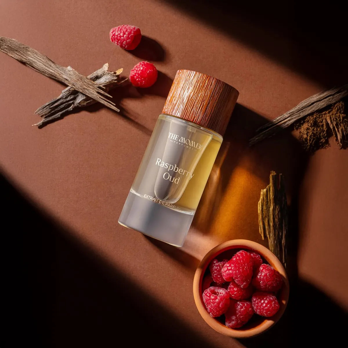 Perfume bottle labeled 'Raspberry Oud' with raspberries and dried herbs on a brown background