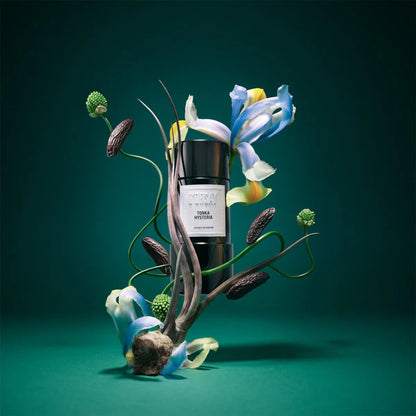 Bottle of tonka bean extract surrounded by flowers and plants on a green background